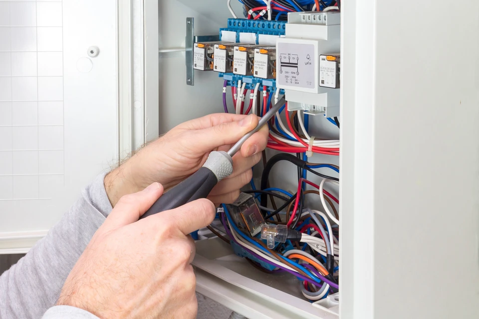 Un électricien travaille dans un tableau électrique ouvert, manipulant un tournevis pour effectuer des réparations ou de la maintenance