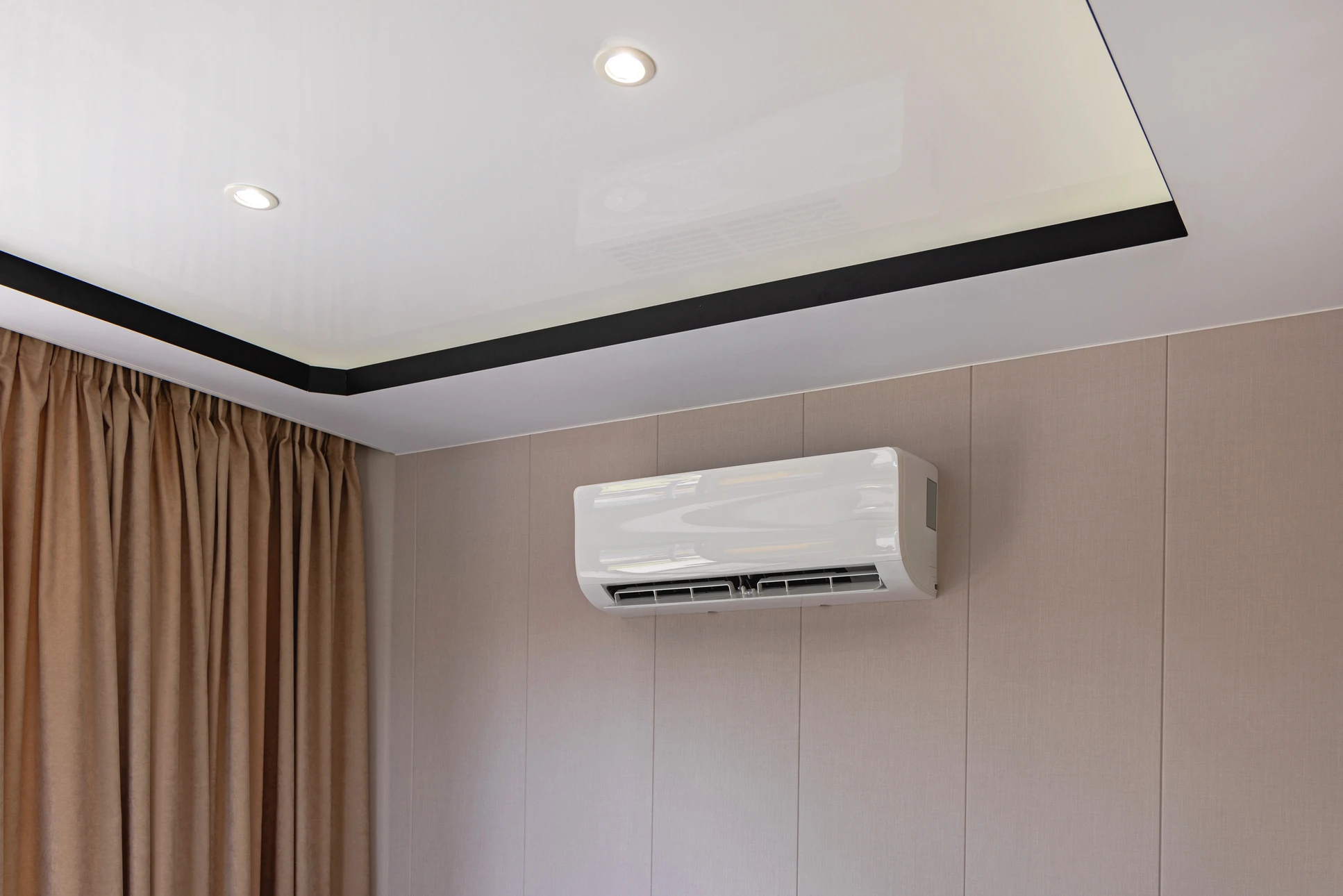 Un technicien en chemise grise installe ou répare une climatisation murale dans un intérieur moderne